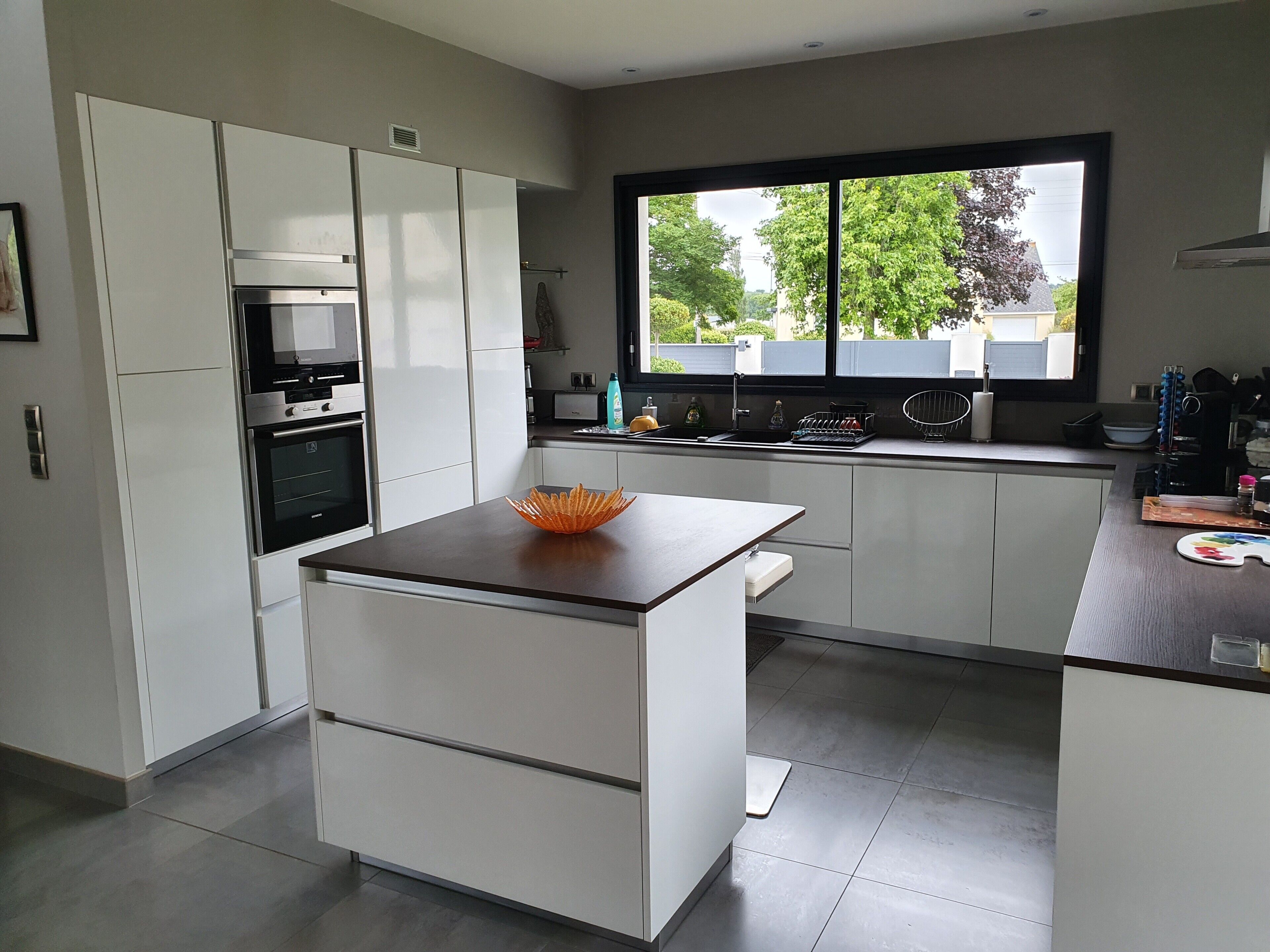 A modern kitchen with white cabinetry, a built-in oven, and a window with a view of trees and buildings.