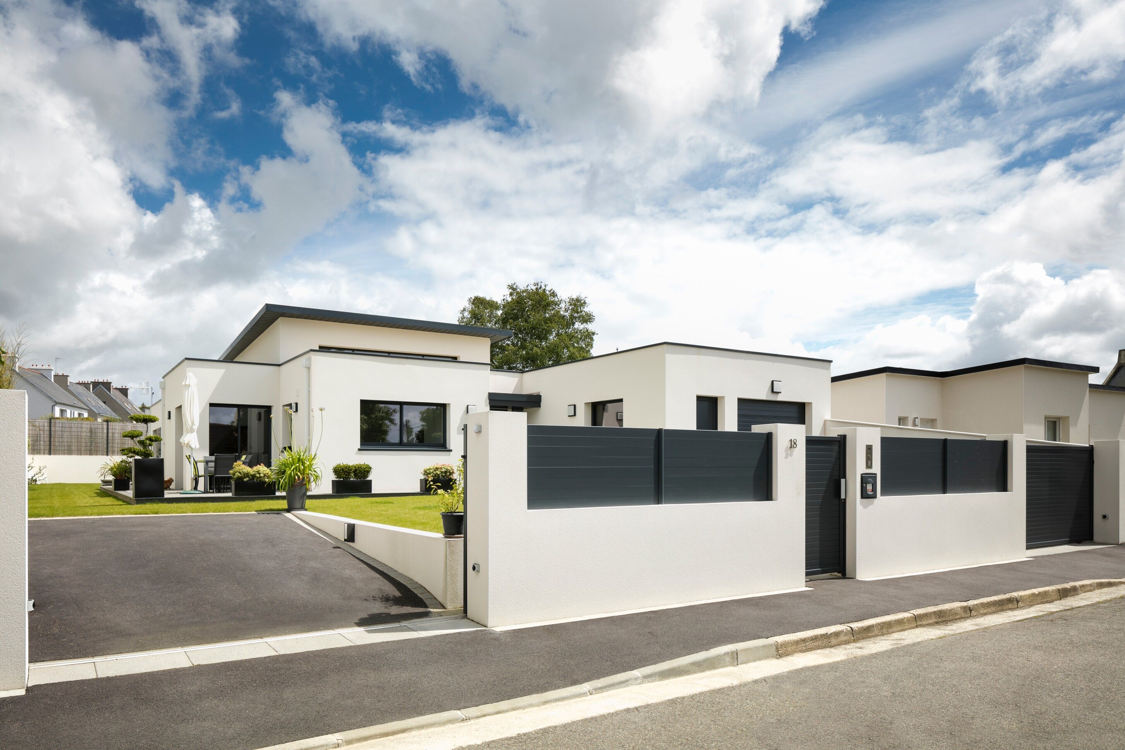 Un quartier résidentiel moderne composé de maisons individuelles, doté d’une allée d’accès fermée par un portail et d’une pelouse bien entretenue.