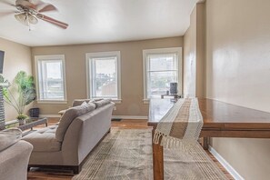 A living room with a sofa, a coffee table, and a ceiling fan. There are three windows with blinds. - Mount Washington 4BR Home, Sleeps 10, 2 Kitchens (Pittsburgh)
