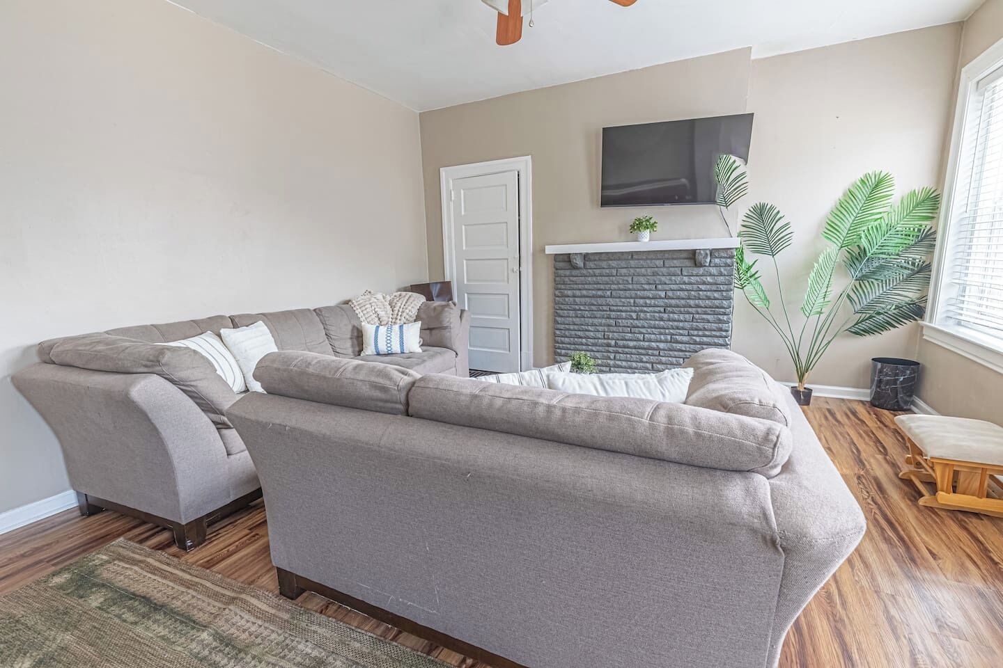 Ein Wohnzimmer mit grauem Sofa, Kamin, Fernseher und einer Topfpflanze.