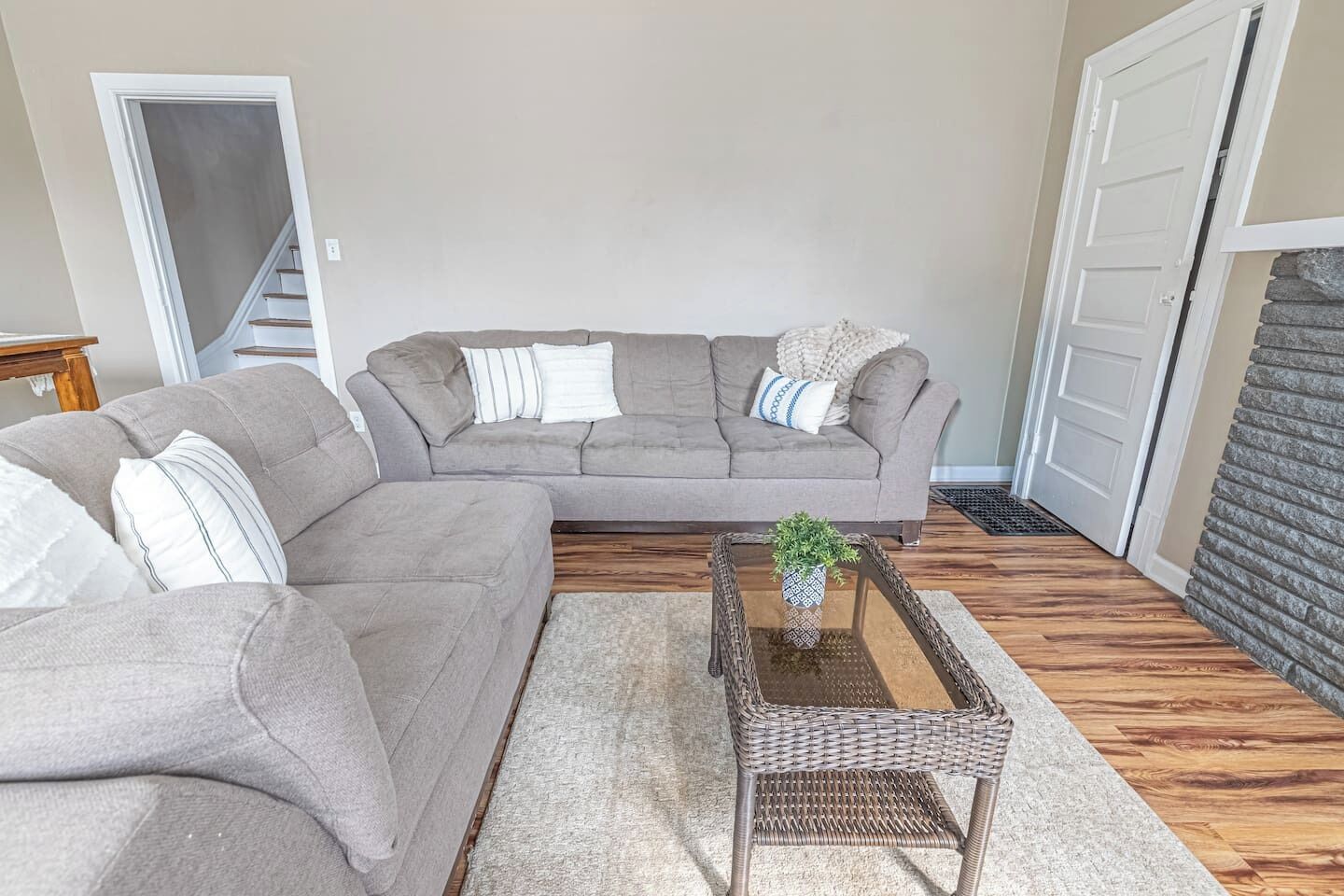 A living room with a grey sectional sofa, a small side table with a plant, and a wooden floor.