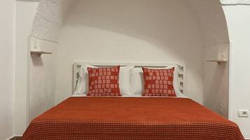 A bed with a red cover, white pillows, and a white headboard under an arched white ceiling.