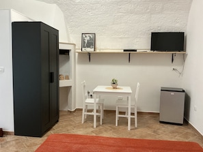 Cocina compacta con refrigerador, una mesita con sillas, una planta en maceta y un televisor montado.