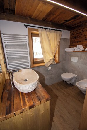 Ein Badezimmer mit einem Holzkosmetikschrank, einem runden Waschbecken, einem Fenster mit Vorhängen und einem Regal mit Handtüchern.