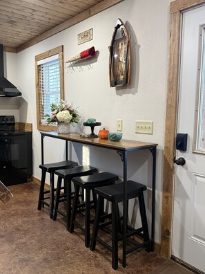 A kitchen with a wooden table, black stools, a stove, and a window with blinds. - Gumm Creek Cabins
Rustic Modern Cabin w/Loft + Trail Access in Mena (Mena)