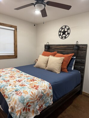 A bedroom with a bed, a ceiling fan, a wall clock, and a window with blinds. - Gumm Creek Cabins
Rustic Modern Cabin w/Loft + Trail Access in Mena (Mena)
