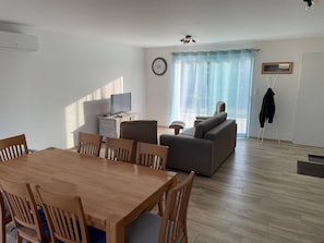 Ein modernes Wohnzimmer mit Essbereich, einer Couch, einem Fernseher und einer Uhr an der Wand.