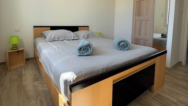 A modern bedroom with a wooden bed, grey bedding, and a green lamp on a bedside table. - New home in the heart of the Médoc—4 bedrooms, garden, beaches 20 minutes away (Lesparre-Médoc)