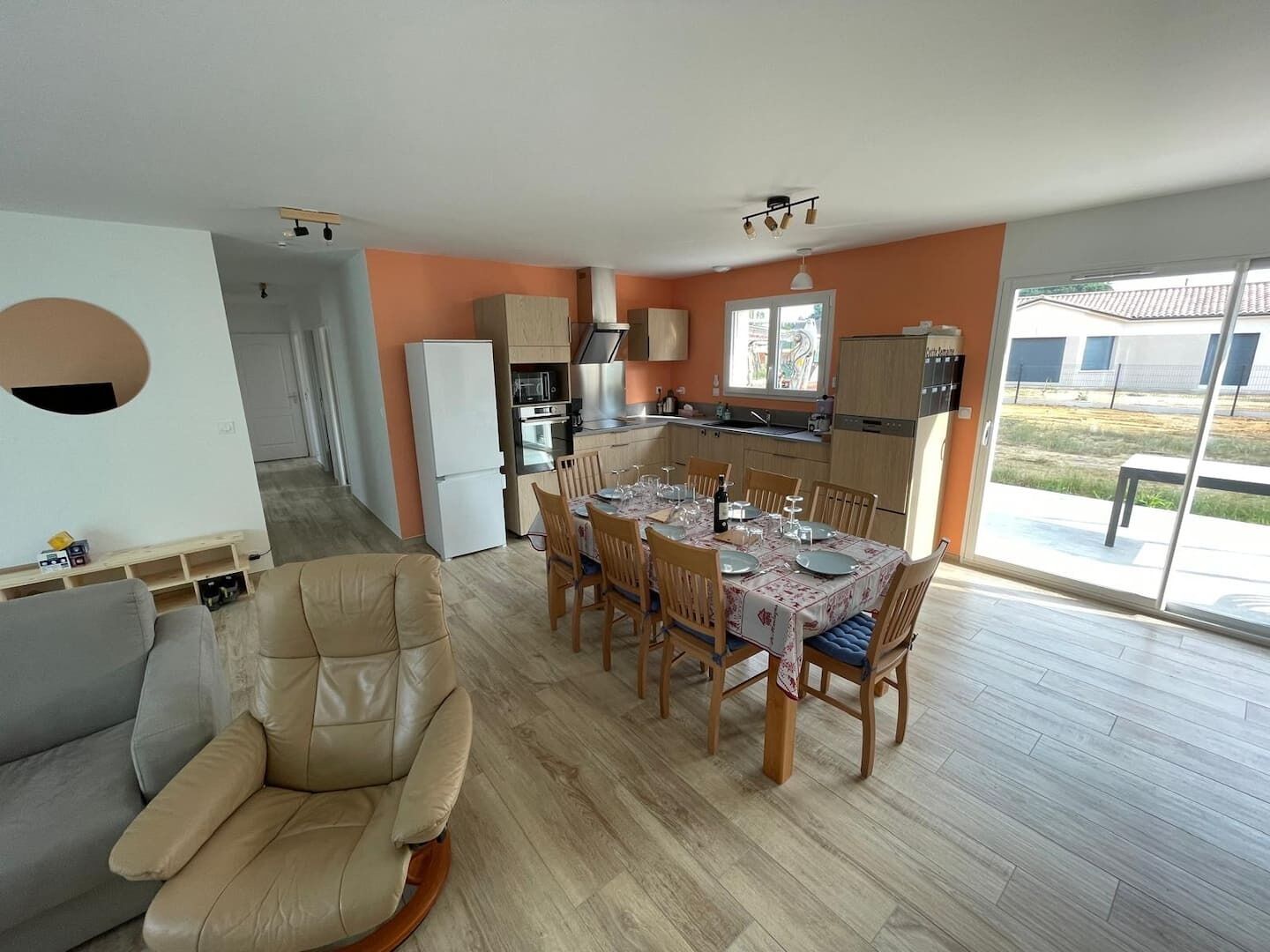 A modern kitchen with a dining area, a sofa, and a view of the outdoors.