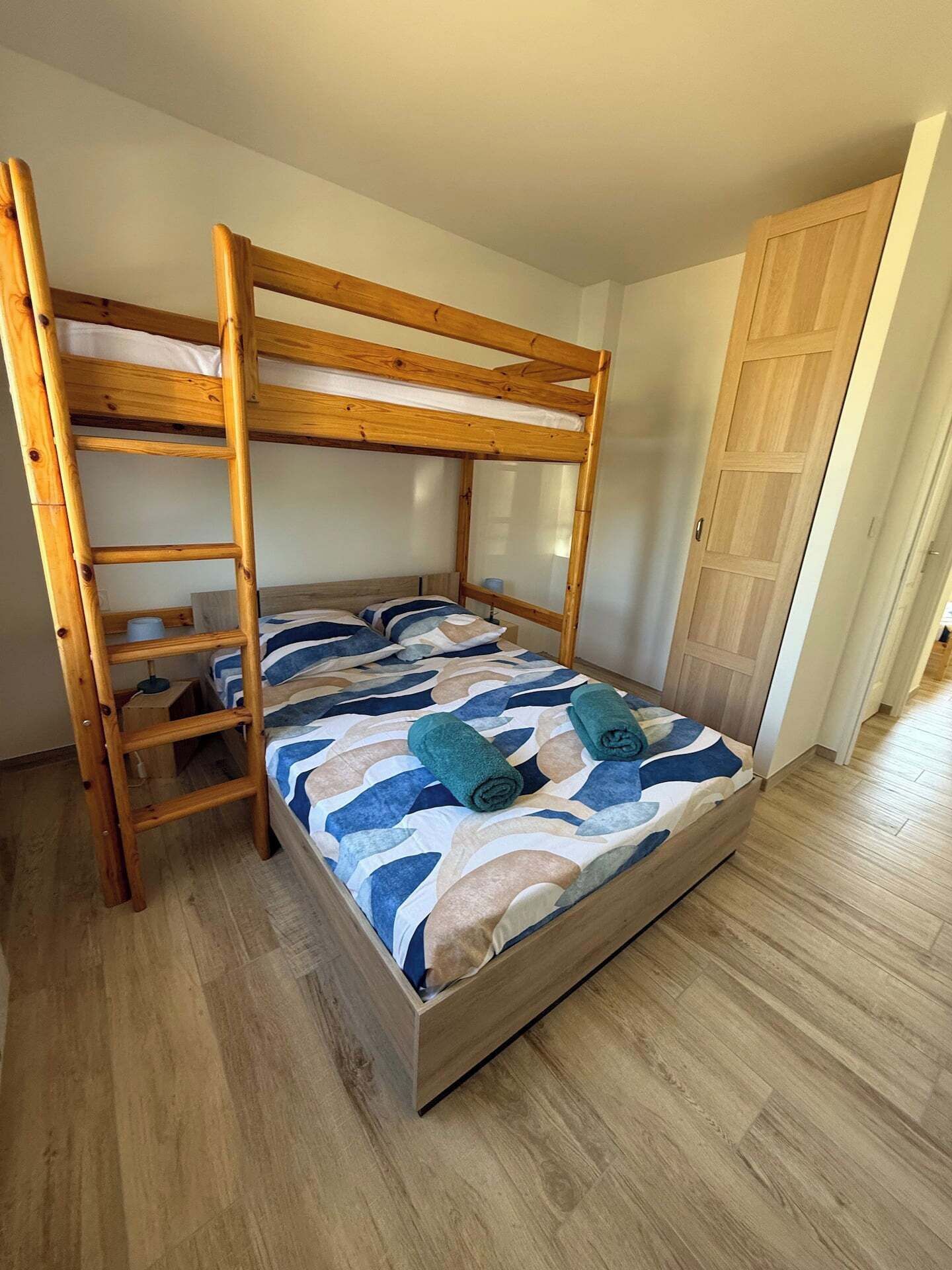 Uma cama beliche com estrutura de madeira e colcha estampada.