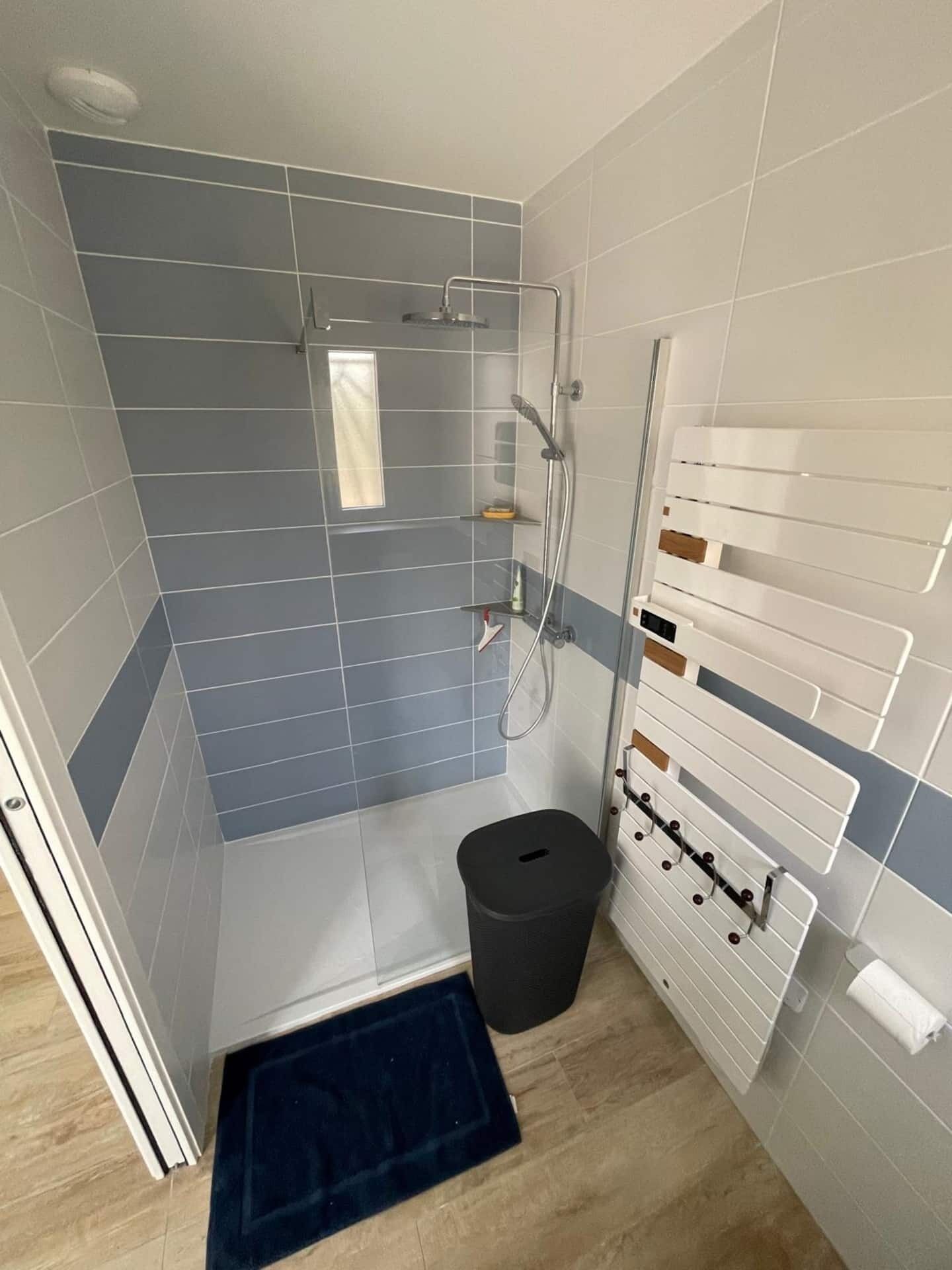 A shower area with a glass door, a small trash bin, and a towel rack.