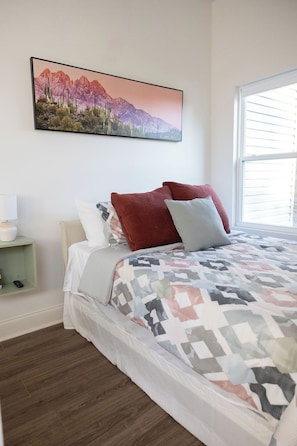 A bedroom with a bed, pillows, a nightstand, a lamp, and a painting of a mountain landscape.