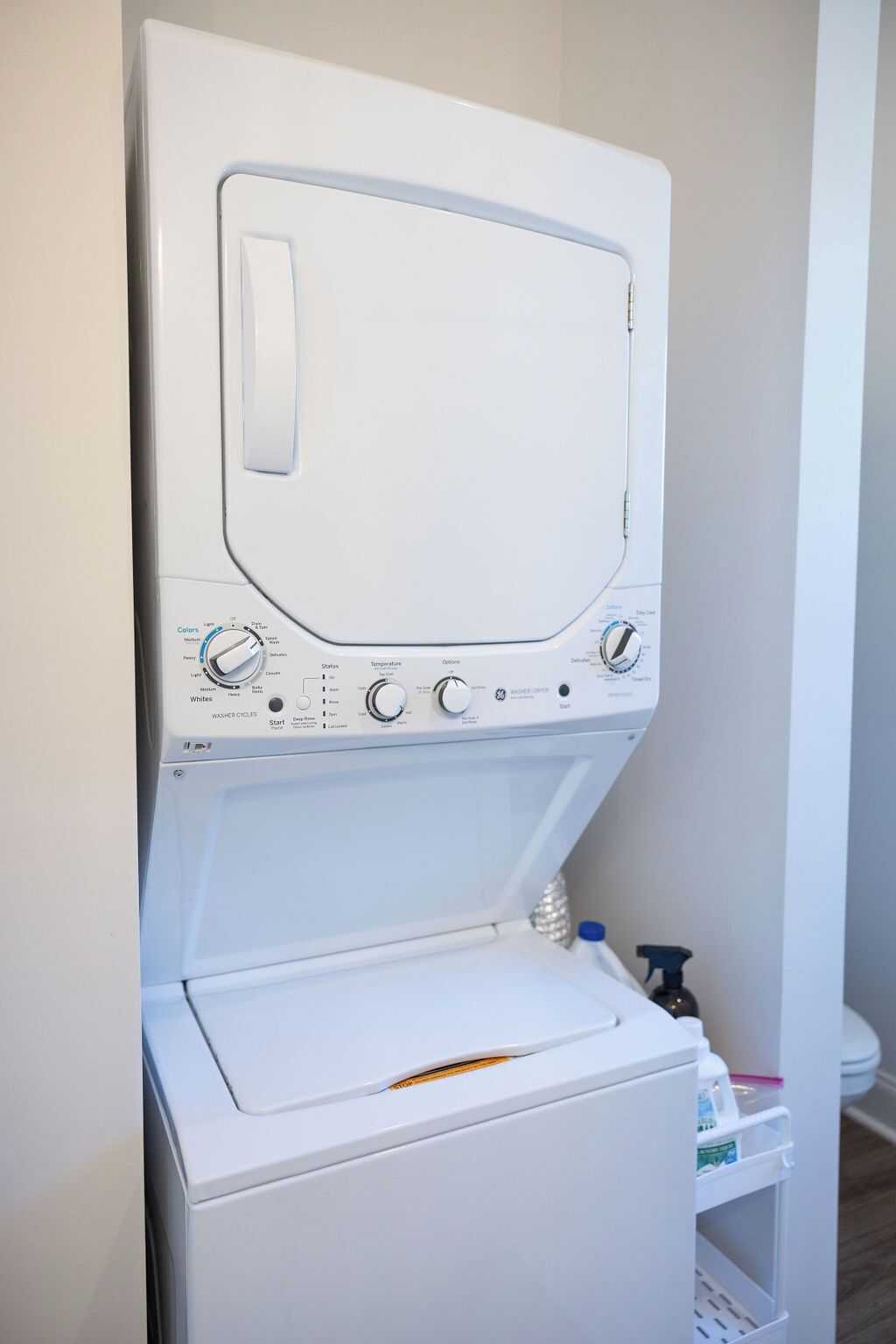 A front-loading washing machine with a control panel, a detergent bottle, and a cleaning product on a shelf.