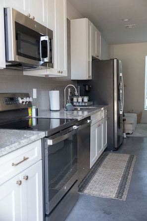 A modern kitchen with stainless steel appliances, white cabinetry, and a patterned rug.