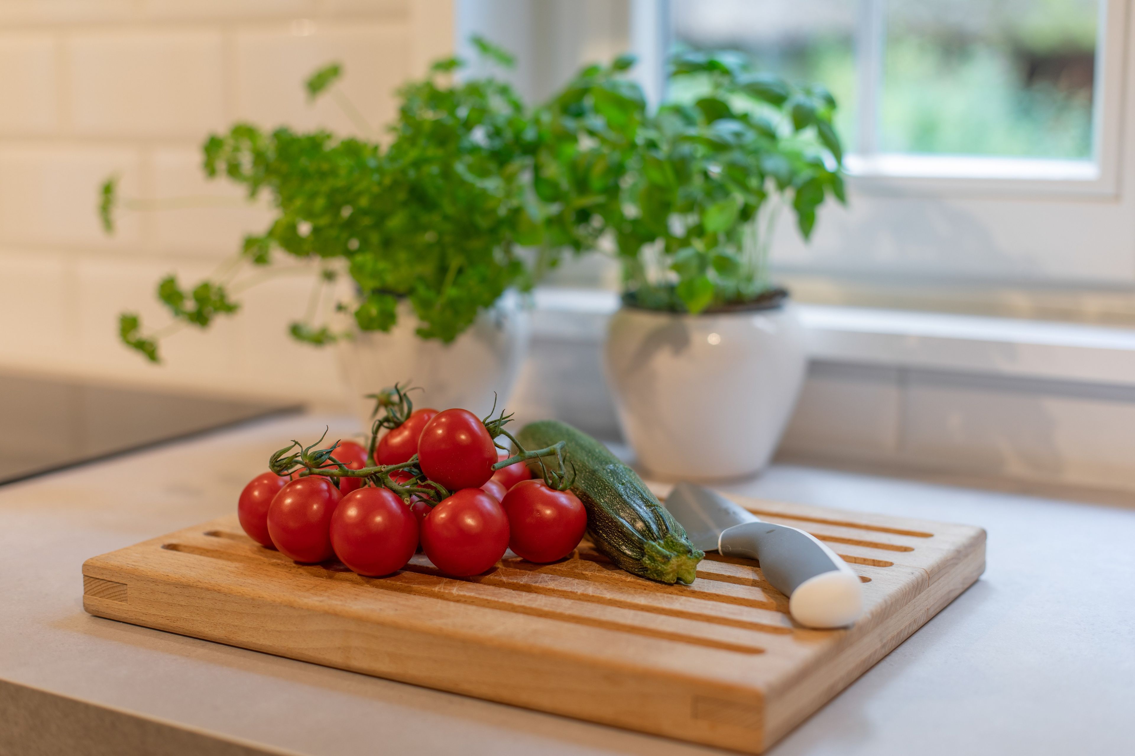 Une planche à découper en bois avec des tomates cerises et une courgette, posée sur un plan de travail de cuisine.