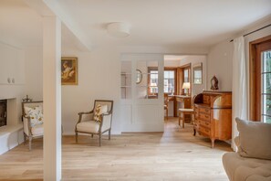 Ein geräumiges Zimmer mit Holzboden, einem klassischen Sessel, einem Holzschrank und einer Tür zu einem anderen Raum.