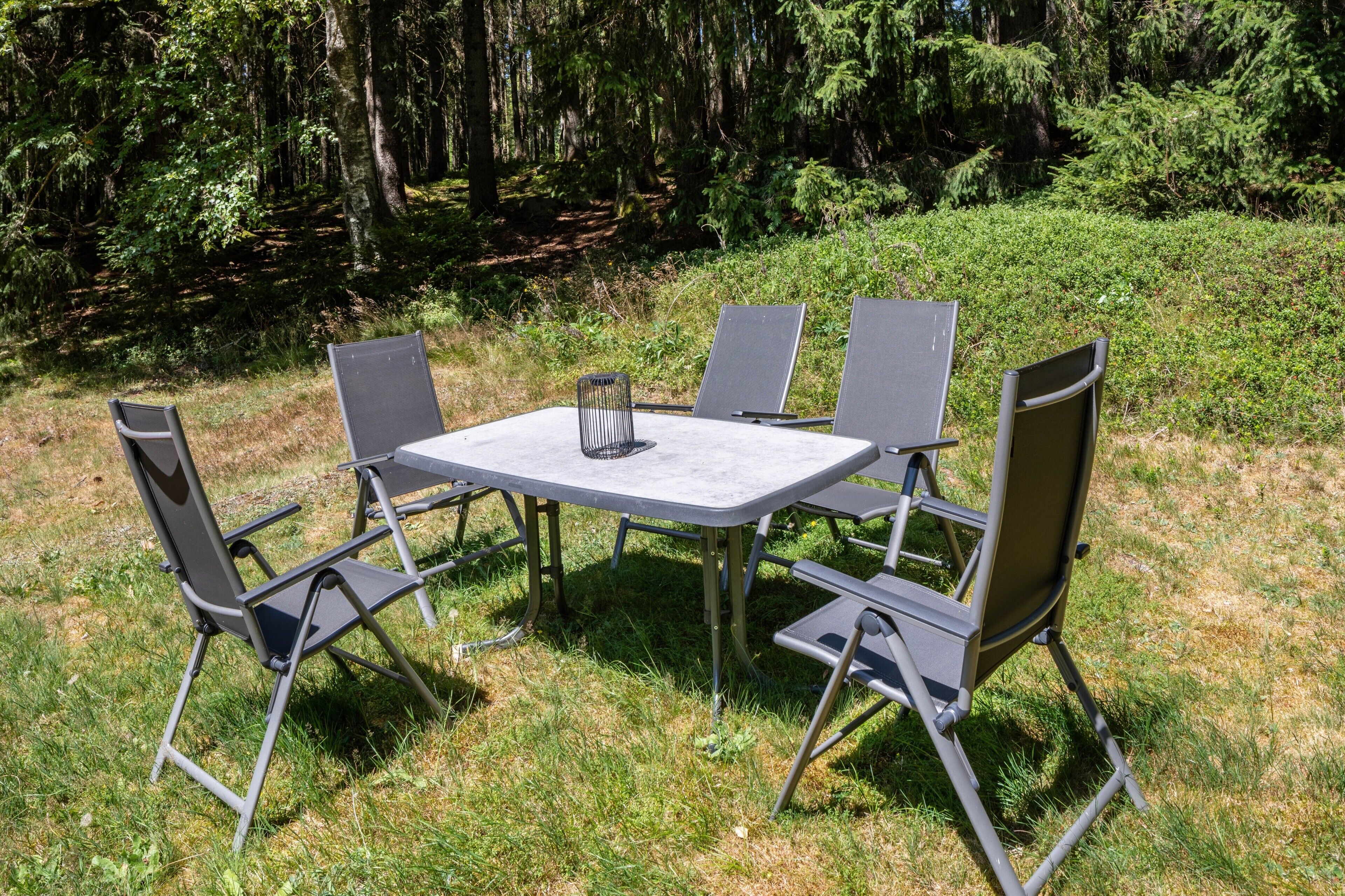 Una mesa y cuatro sillas colocadas al aire libre, con un césped y árboles al fondo.