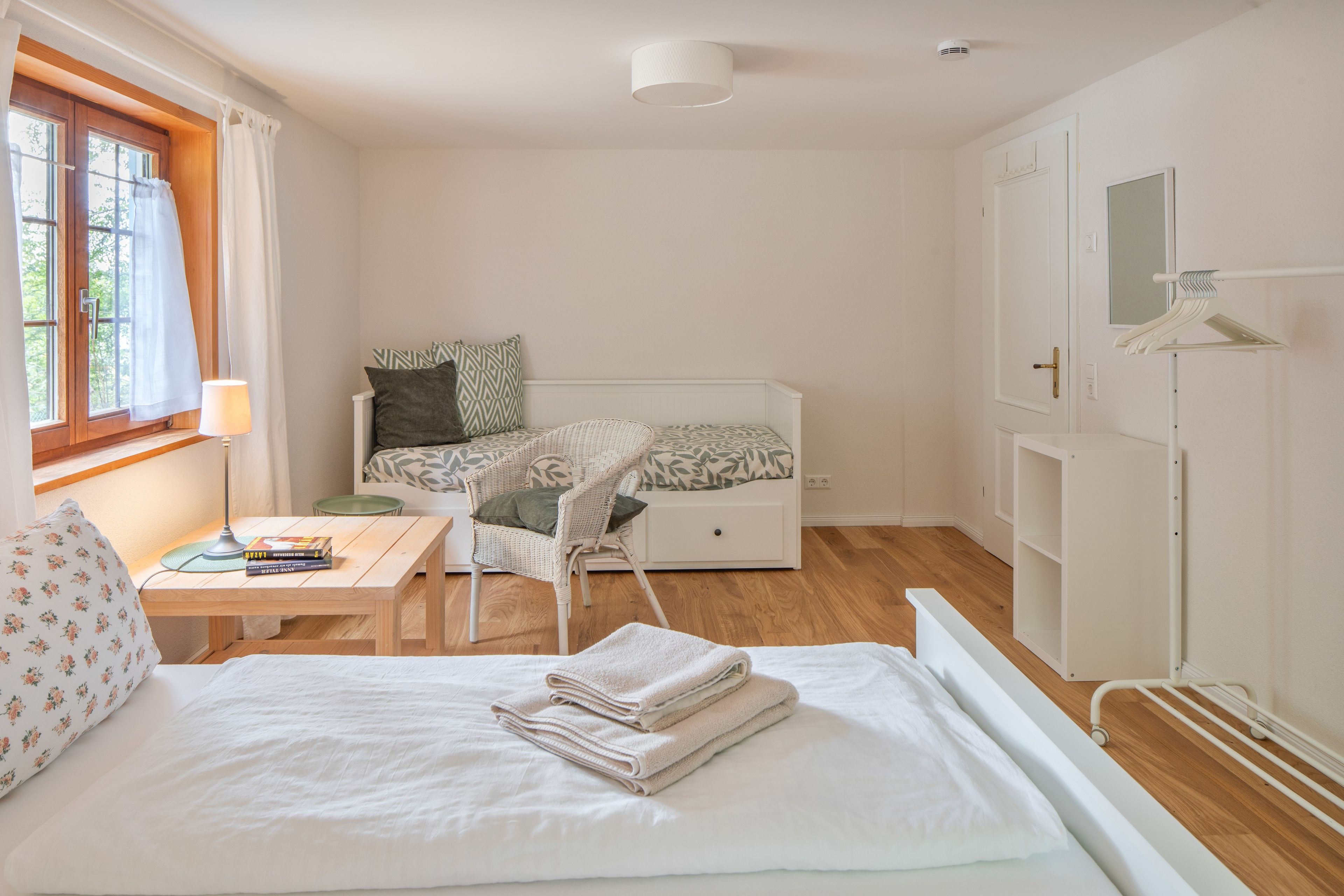 Ein Schlafzimmer mit Bett, Sessel, Schreibtisch und Fenster.