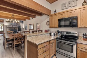 A kitchen with wooden cabinets, a granite countertop, a built-in oven, a microwave, and a dining area with a wooden table and chairs. - 2BR + Loft Condo | Shared Pool & Shuttle Access (Mammoth Lakes)