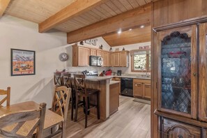 A kitchen with wooden cabinets, a dining area with wooden chairs, a built-in microwave, and a large wooden cabinet with glass doors. - 2BR + Loft Condo | Shared Pool & Shuttle Access (Mammoth Lakes)