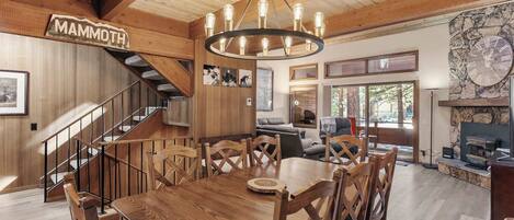 A wooden interior with a dining table, chairs, a staircase, and a stone fireplace.