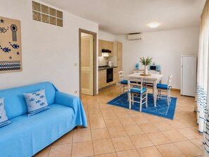 Ein gemütlicher Wohnbereich mit einem blauen Sofa, einem Esstisch mit Stühlen, einer Küchenzeile und einem weißen Kühlschrank.