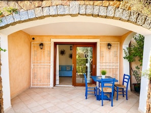 A covered patio area with a stone archway, a table with chairs, and a view into the interior. - GioYa House – Three-room apartment with a garden, 100 meters from Pittulongu Beach (Pittulongu)