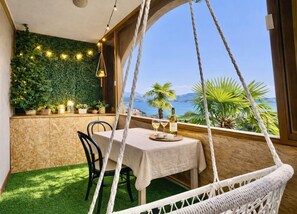 A dining area with a table set for two, a hanging chair, and a view of the sea. - 180° View of Lake Maggiore and the Alps (Meina)