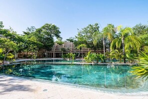 A clear swimming pool surrounded by lush greenery and a multi-story building in the background. - Luxury 4BR Villa in Tulum | Jaguar Park & Beach (Tulum)