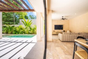 A modern living space with a pool, outdoor seating, and a TV in the living area. - Luxury 4BR Villa in Tulum | Jaguar Park & Beach (Tulum)