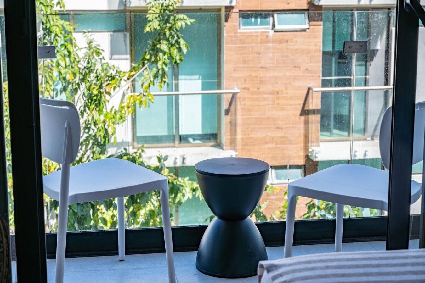 A balcony with two white chairs and a black table, overlooking a brick building and greenery.