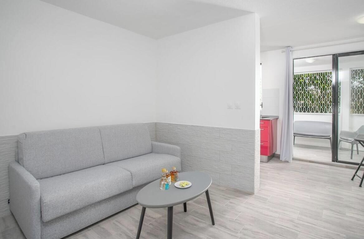 Una sala de estar moderna con un sofá gris, una mesa redonda pequeña y una cocina visible a través de una puerta abierta.