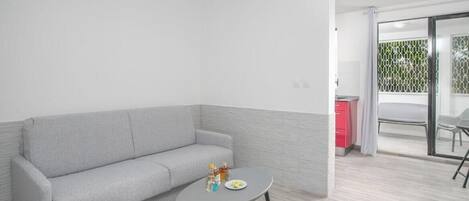 Una sala de estar moderna con un sofá gris, una mesa redonda pequeña y una cocina visible a través de una puerta abierta.