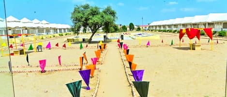 A sandy outdoor area with tents and colorful flags arranged in rows.