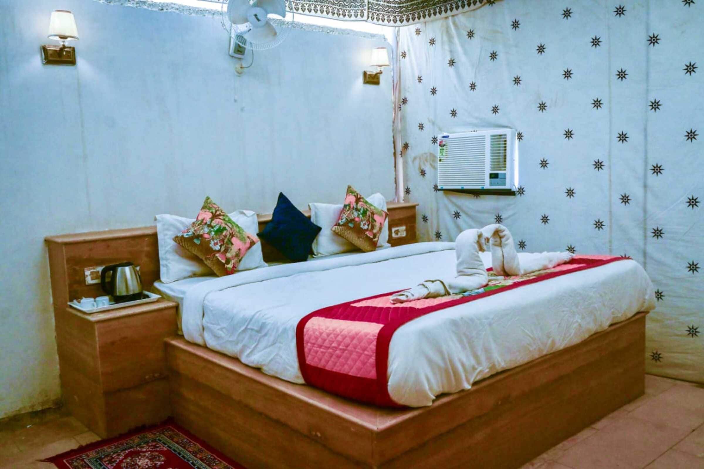 Un dormitorio con una cama de madera, una mesita de noche con hervidor, aire acondicionado en la pared y una cortina estampada.