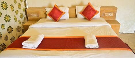A double bed with a red and white bedspread, two nightstands with wooden drawers, and a patterned curtain.