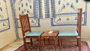 Una habitación con pared de diseño, una silla de madera con cojín, una pequeña mesa de madera y una alfombra estampada.
