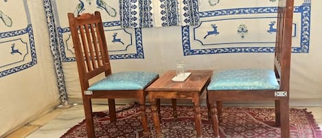 A room with a patterned wall, a wooden chair with a cushion, a small wooden table, and a patterned rug.