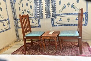 Una habitación con pared de diseño, una silla de madera con cojín, una pequeña mesa de madera y una alfombra estampada.