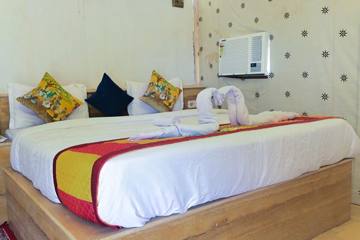 A bed with a white and red bedspread, two pillows, and a wall-mounted air conditioner.