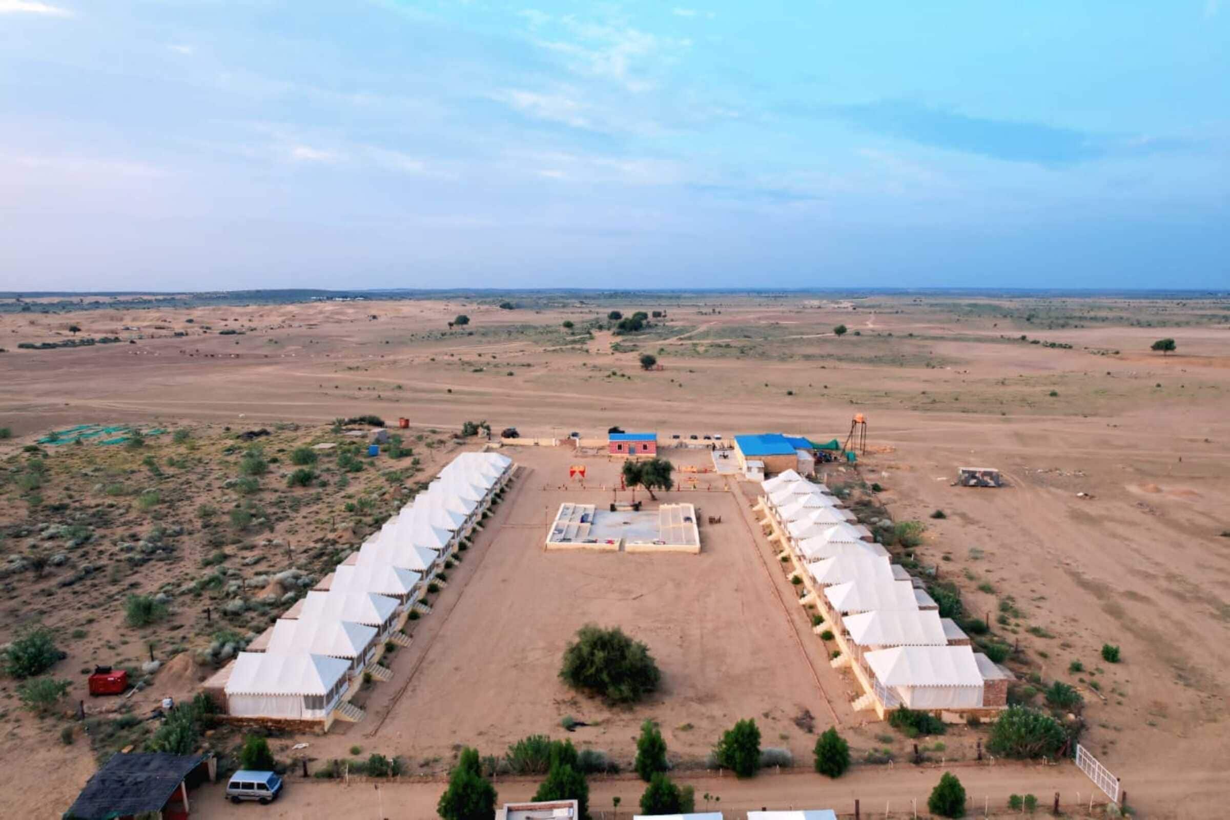 A large, open area with a central building surrounded by tents, set in a desert landscape.