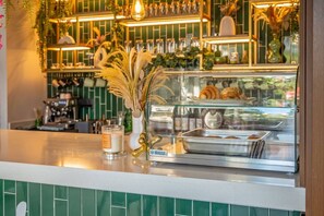 A cafe counter with a glass display case containing pastries, a candle, and a decorative vase. - Modern Studio | Gym + Rooftop Pool, Free Parking (Playa del Carmen)