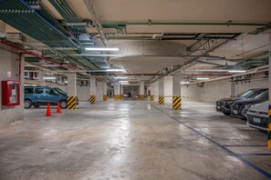 A multi-level underground parking garage with concrete pillars, fluorescent lighting, and marked parking spaces. - Modern Studio | Gym + Rooftop Pool, Free Parking (Playa del Carmen)