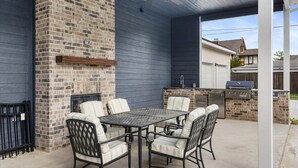 Eine Terrass mit Kamin aus Backstein, Grill und Esstisch mit Stühlen.