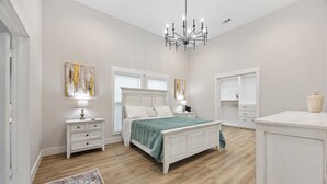 Ein Schlafzimmer mit Bett, Nachttischen, einer Chandelier, einem Kleiderschrank und einem Teppich.