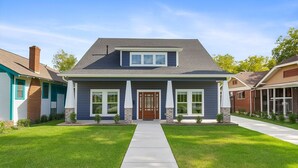 Ein zweistöckiges Haus mit Veranda, einer mittleren Tür und einem kleinen Vorgarten.