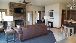 A living room with a stone fireplace, a brown leather sofa, a television, and a ceiling fan. - Spacious 4BR Lake House on Gull Lake - Fireplace & Sunset Views (Brainerd)