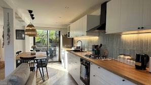 A modern kitchen with white cabinetry, a wooden countertop, and a dining area with a sofa and chairs. - Newly remodeled house just steps from the beach and the wetland (La Laguna)