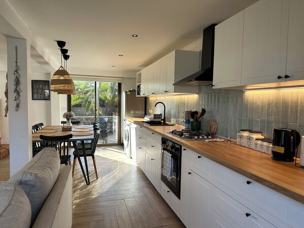 A modern kitchen with white cabinetry, a wooden countertop, and a dining area with a sofa and chairs. - Newly renovated house just a few steps from the beach and wetlands (La Laguna)