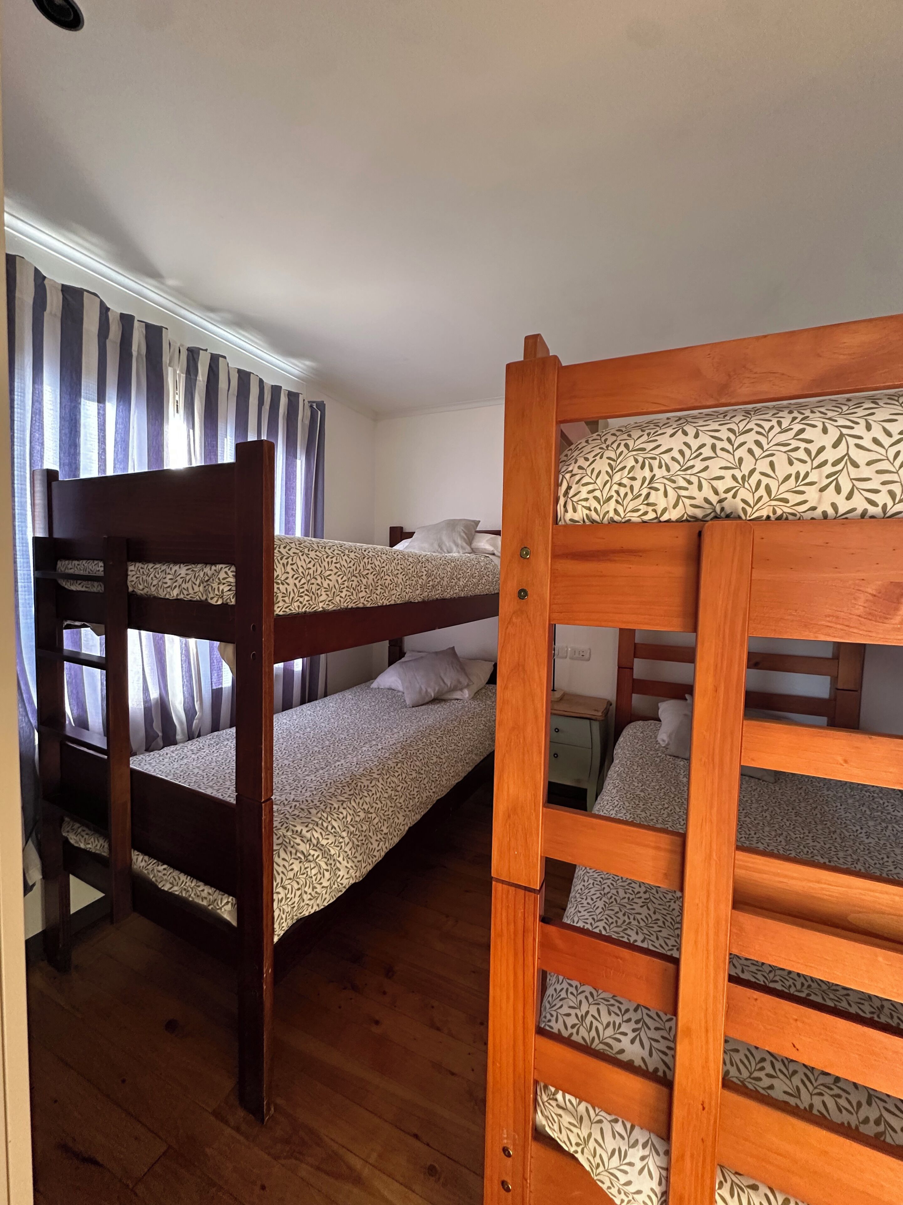 Habitació amb dos llits superposats, una finestra amb cortines i un terra de fusta.